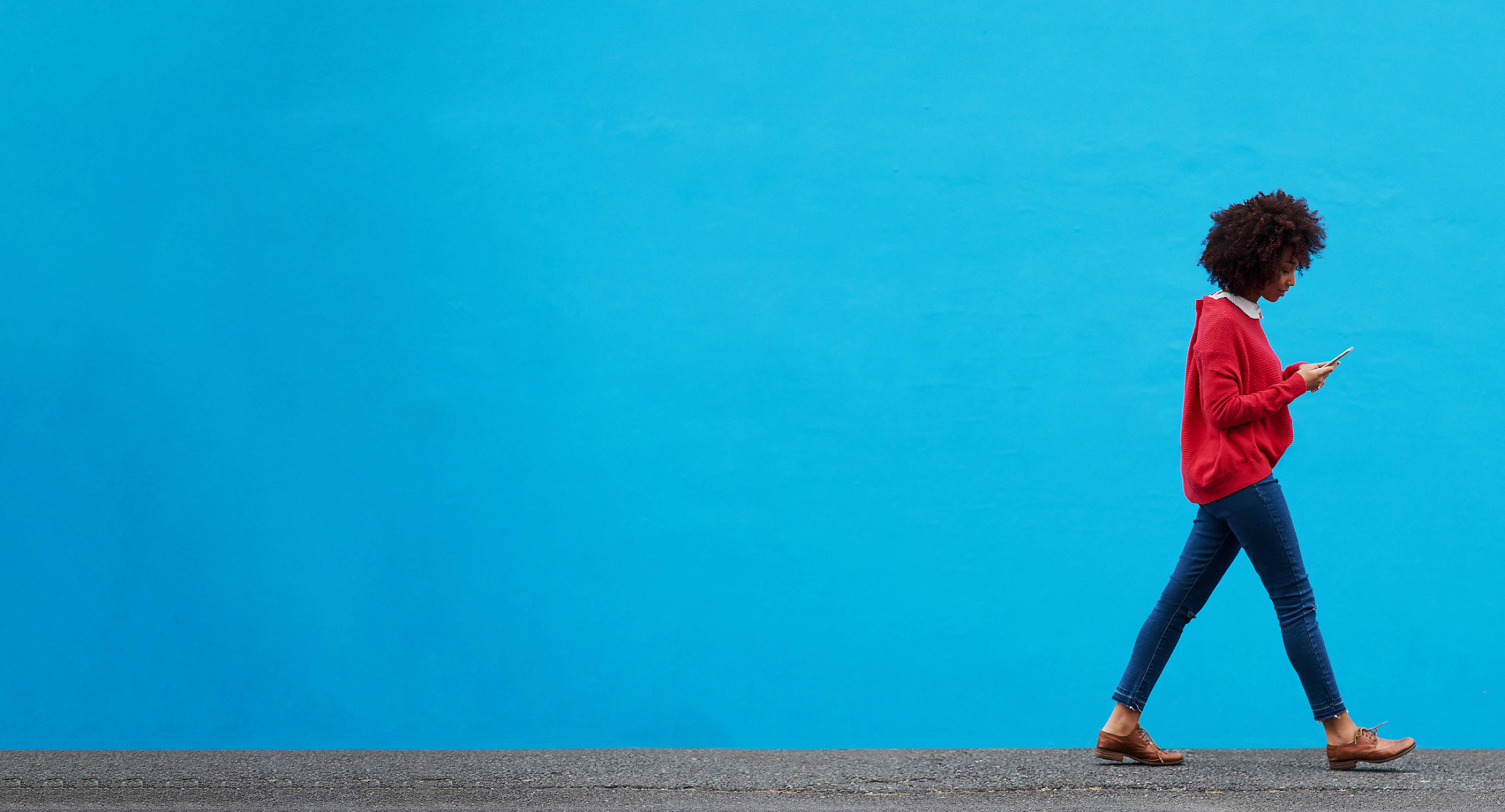 Woman walking in the bottom right hand corner of a blue backdrop